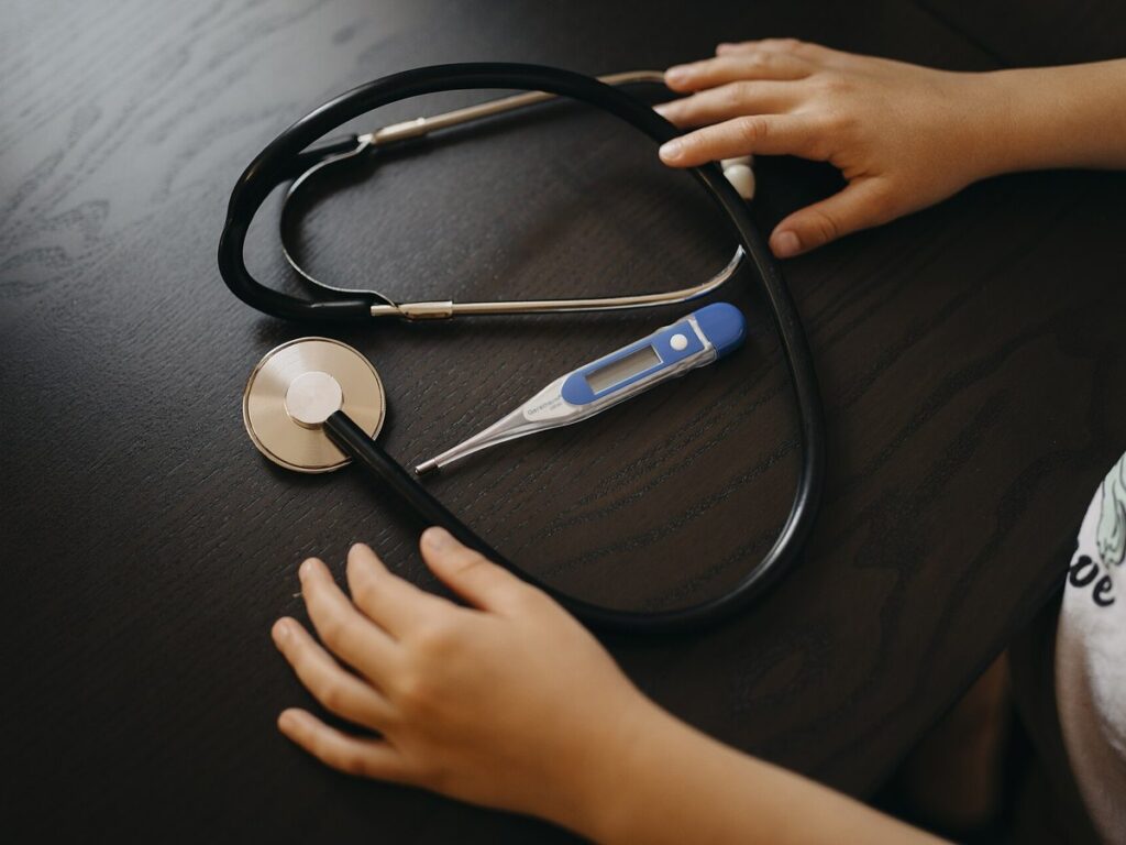 Hands of a child reach for a stethoscope and thermometer on a table in a healthcare environment undefined
